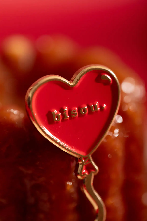Bisou Enamel Pin - Macro shot of the gold-plated "bisou" lettering on red enamel.