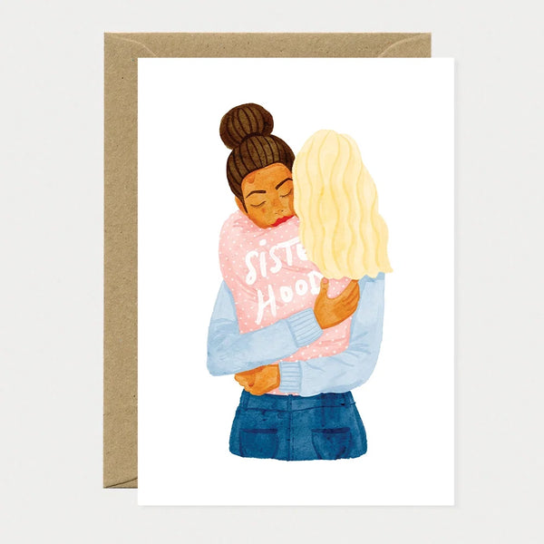 Illustrated greeting card of two women embracing, one wearing a pink sweater with "Sisterhood" written on it and her eyes closed