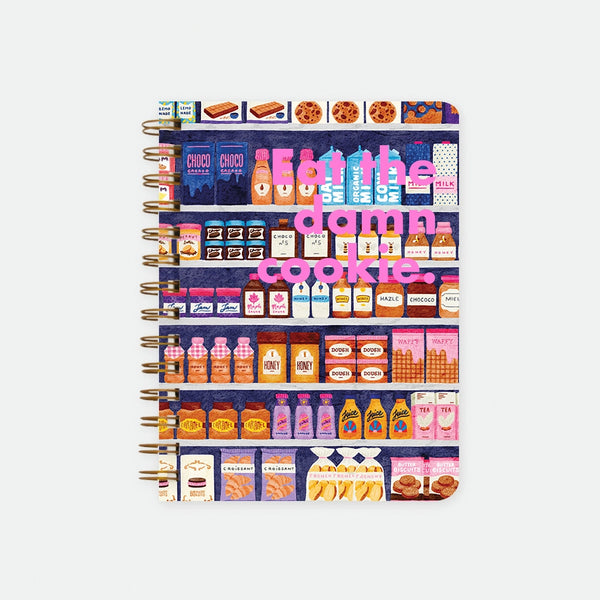 Sugar Market A5 spiral notebook by All The Ways To Say, illustrated grocery shelves packed with jams, milk and biscuits with "Eat the damn cookie." text in pink lettering across the middle, spiral binding visible on the left edge