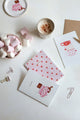 Together Cats collection – pink and white notebooks with red hearts and cat illustration, styled with marshmallows, coffee and stationery clips.