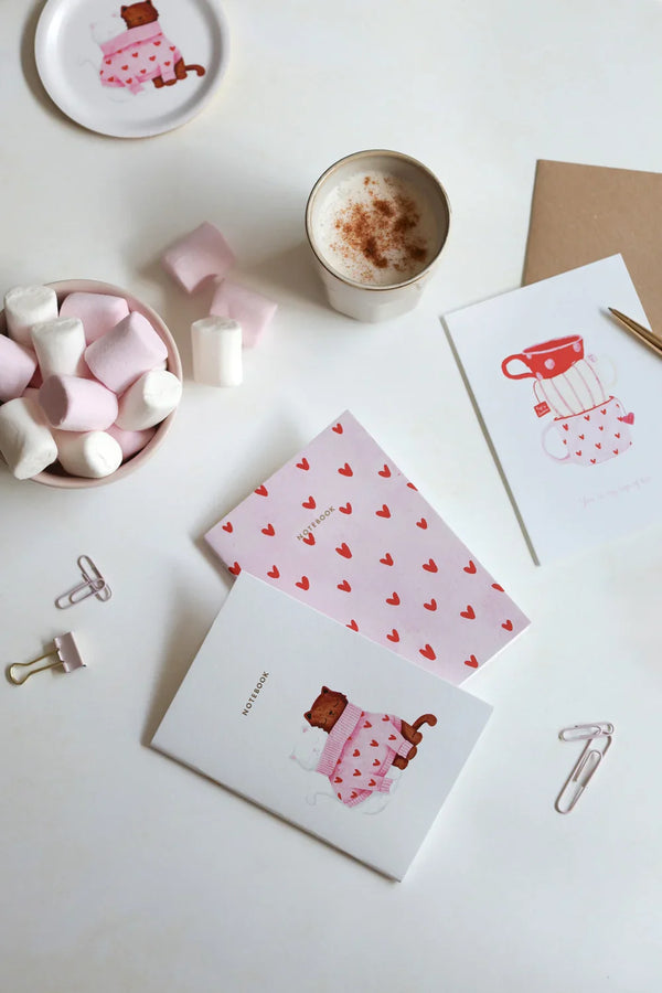 Together Cats collection – pink and white notebooks with red hearts and cat illustration, styled with marshmallows, coffee and stationery clips.