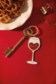"Wine not" enamel keychain shaped like a glittery wine glass with a red heart, next to a gold key and pretzels on a red background