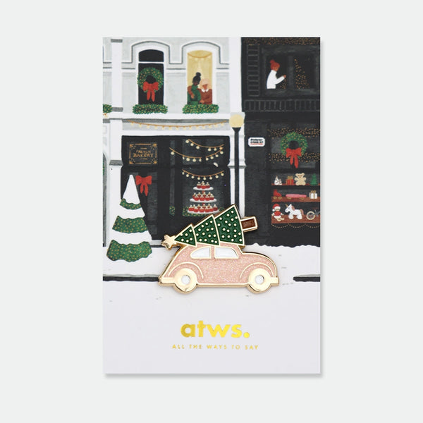 Enamel pin of a pink car with a Christmas tree and gold star strapped to the roof